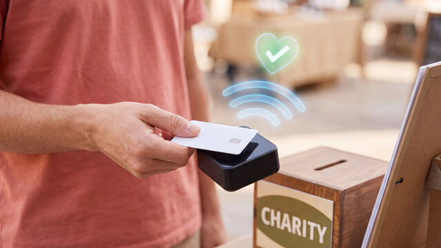 Contactless Charity Donation and Cashless Giving Concept, man tapping card on reader beside charity box with heart, contactless waves and checkmark icon for digital donation and fundraising
