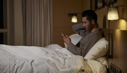 Fototapeta premium Man in Bed Using Phone with Neck Pain at Night