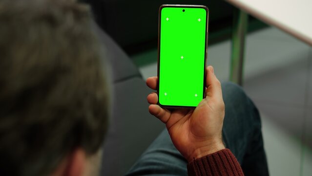 Man holding smartphone with green screen and tracking markers close up over shoulder view. Mobile phone mockup display chroma key space for application web template. Digital device usage