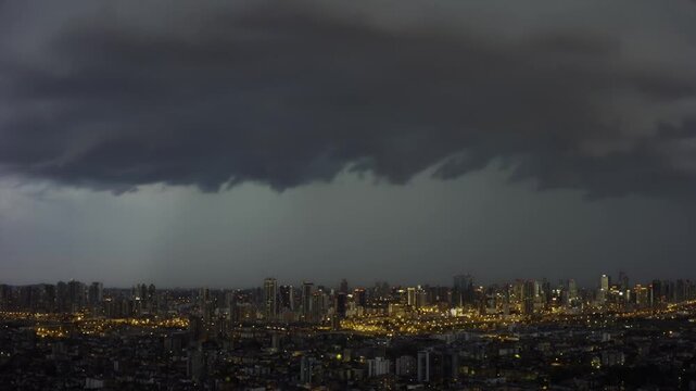Dark storm clouds gather over a city skyline at night, illuminated by city lights, creating a dramatic contrast against the ominous sky