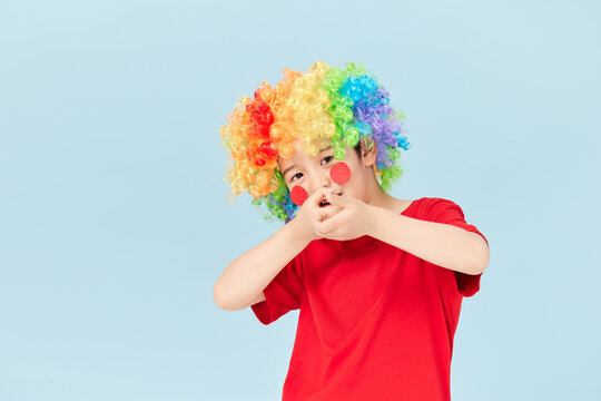 Playful little boy dressed as a clown with rainbow wig on blue background