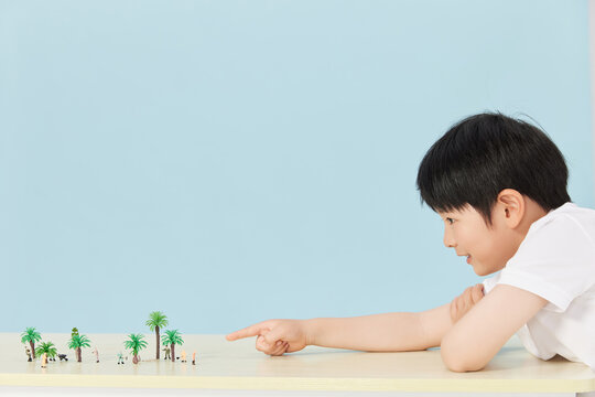 Young boy pointing at miniature palm trees and tiny figures on table