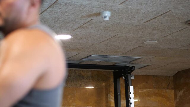 Close-up dynamic shot of an athletic man intensely straining during cable rope face pulls workout in a modern indoor fitness center
