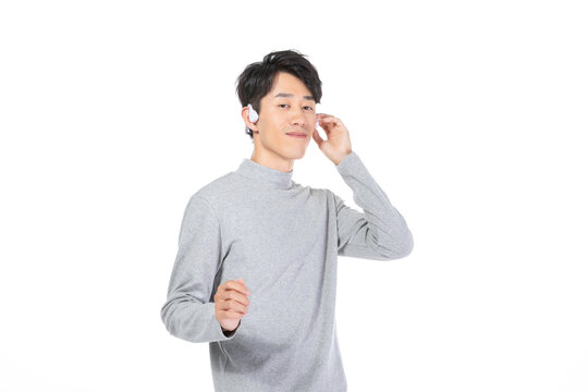 Young man listening with wireless earbud in white studio
