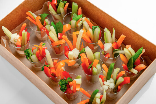 Individual vegetable stick cups in delivery box. Raw sliced vegetables stand upright in small cups served with dip inside a takeaway tray.