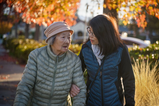 Elderly mother and adult daughter talking while walking. Golden autumn leaf colour in the background. California.
