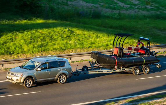 SUV Towing Rescue Boat on Highway at Sunset, Concept of Water Craft Transportation