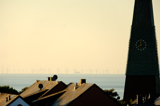 Offshore Wind Farm on Sea Behind Coastal Town and Clock Tower at Golden Hour