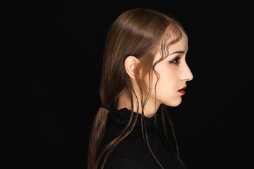 Moody side profile portrait of young woman with wet-look hair on black background © VuXuan