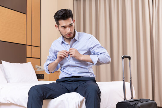 Businessman getting dressed in hotel room beside suitcase during business trip