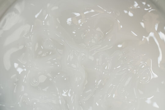 Macro top view of white cosmetic cream texture with soft wavy pattern and glossy light reflections, full frame smooth moisturizer background for luxury skincare concepts.