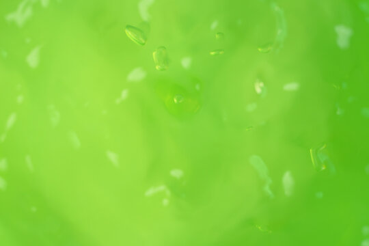 Macro shot of green aloe vera gel texture with air bubbles and light reflections, selective focus with copy space on green background for skincare cosmetics, hydration, and organic beauty products.