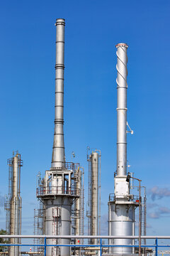 Industrial steel smoke stacks and distillation columns at a petrochemical refinery plant under a clear blue sky