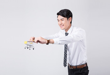 Smiling businessman pushing miniature shopping cart on light background © ChauBich