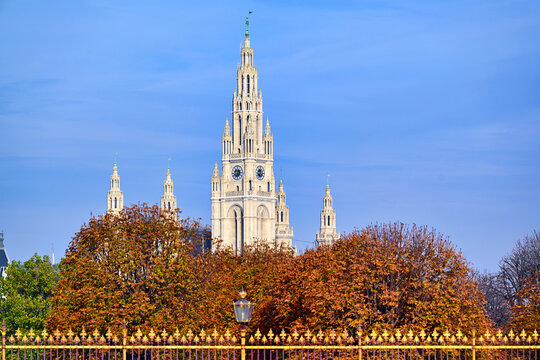 The majestic central tower of Vienna City Hall rising above autumn trees and the gilded fence of Volksgarten, Vienna