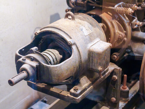 Close-up of a vintage industrial electric motor with rusted metal housing. Detailed view of old mechanical components, shafts, and bolts in a factory setting. Antique heavy machinery equipment.