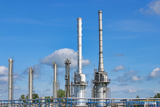 Wide scenic landscape of a petrochemical refinery plant with metallic distillation columns and smokestacks under a blue sky