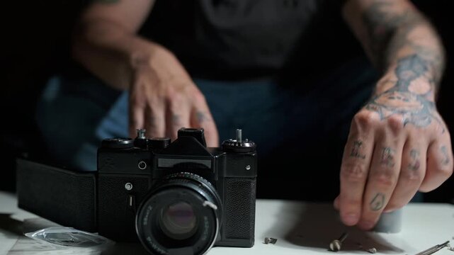 Tattooed male hands disassembling and repairing an old analog film camera. Professional technician working on vintage photographic equipment