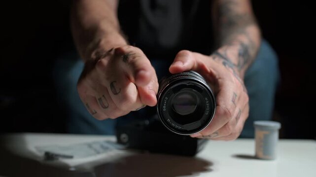 Male technician with tattooed hands carefully checking and adjusting a vintage manual focus lens for an analog slr film camera at a work table