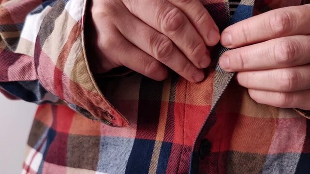 Woman fastens a button on her plaid shirt, getting dressed, everyday fashion, morning preparation, personal routine.