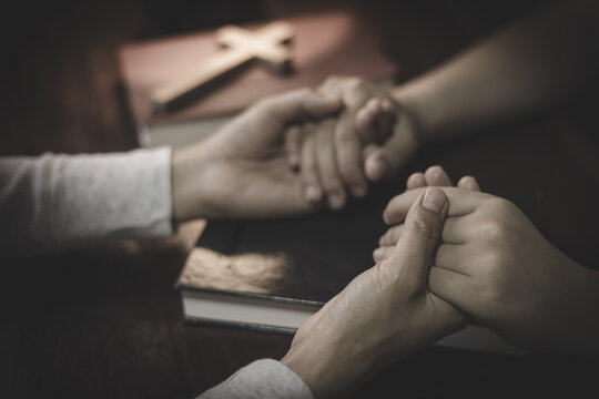Two people praying together and holding hands, expressing faith, love, trust, hope, and spiritual support.