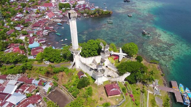 Aerial view of Batu Lubang, Lembeh Island in Bitung, Indonesia. The iconic Trikora Monument stands tall above a vibrant fishing village and boats moored in crystal-clear turquoise waters.
