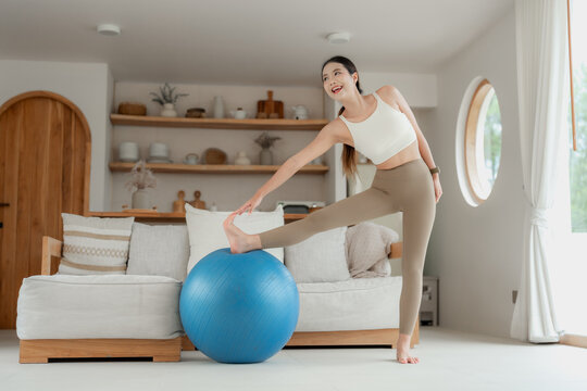 Asian woman stretching leg on exercise ball in living room