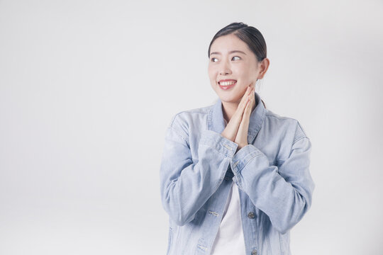 Hopeful young woman in denim jacket smiling with clasped hands