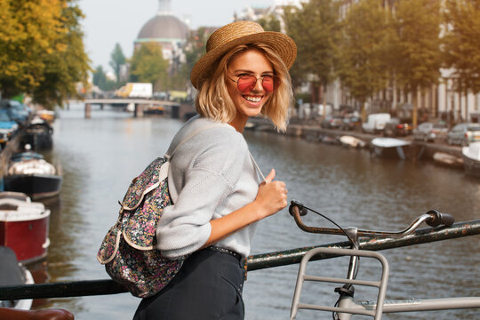 Happy traveler girl enjoying Amsterdam city. Smiling woman on Amsterdam canal, Netherlands, Europe