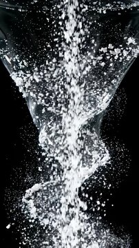 White Granules Falling Into a Water Vortex Against a Black Background