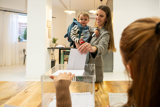 Mother holding her child while casting a ballot into a clear election box