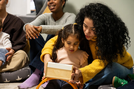 Teacher and little girl sitting on floor, learning with a wooden educational toy