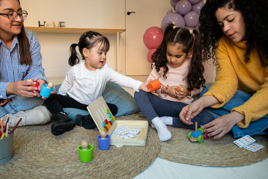 Teachers and young children engaging in educational play activity on the floor with colorful wooden toys