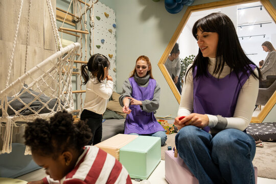 Teachers engaging with young diverse children during playtime in a modern early education center
