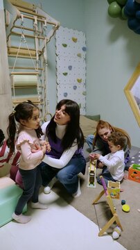 Caring teacher comforting a sad little girl while other children are playing in a modern kindergarten