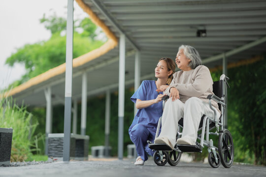 Senior Asia women in a wheelchair sits in the garden, closely attended by a caregiver at a nursing home.