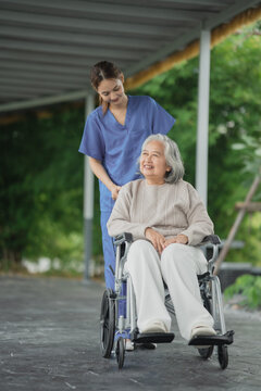 Young woman pushes an old lady in a wheelchair through a park
