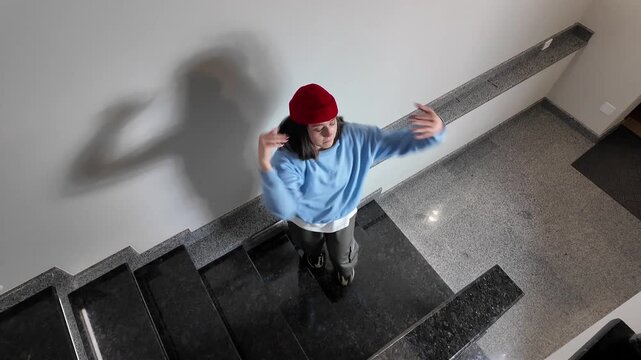 Young Woman in Red Beanie Freestyle Dancing Hip Hop on a Staircase in a Modern Building Lobby