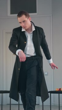 Dancer executes fluid motion against light colored wall. Right hand lifts to chest level as subject looks upward. Two small tables flank subject holding red yellow apples