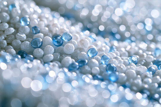 Close-up macro shot of tiny white and translucent blue plastic granules, likely PP (polypropylene) and ASA (acrylonitrile styrene acrylate) polymers, forming an abstract industrial