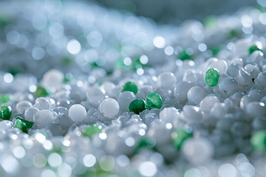Close-up of white and green plastic granules, specifically PP (Polypropylene) and ASA (Acrylonitrile Styrene Acrylate) polymer pellets, forming an abstract background texture with a soft