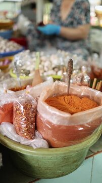 Close-up of ground orange turmeric powder and chili spices in plastic bags with a spoon displayed in a bowl on a stall at Xom Moi Market in Nha Trang, Vietnam. Commercial food supply and retail trade.