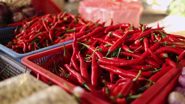 Close-up of fresh red chili peppers displayed in plastic baskets on a market stall at Xom Moi Market in Nha Trang, Vietnam. Commercial food supply, spice market and retail trade concept.