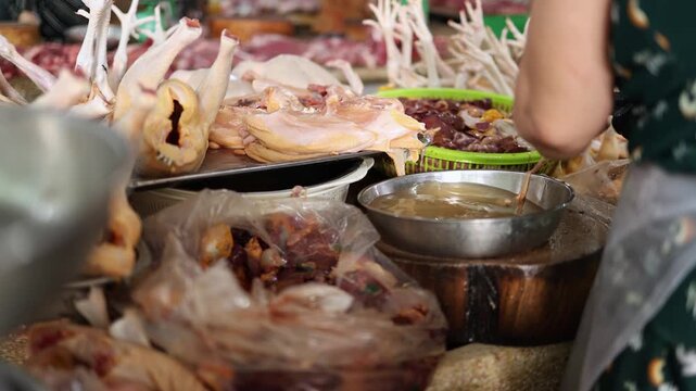 Close-up of a vendor in black gloves washing raw chicken parts and offal in a steel bowl at a stall in Xom Moi Market in Nha Trang, Vietnam. Commercial food supply and retail trade concept.