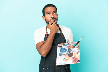 Young artist latin man holding a palette isolated on blue background having doubts © luismolinero