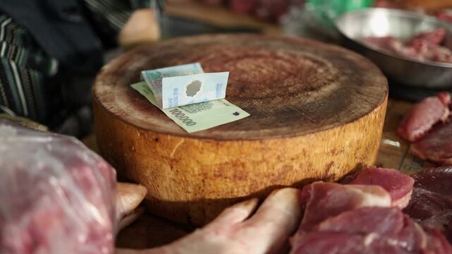 Close-up of Vietnamese dong banknotes placed on a wooden chopping block surrounded by raw meat at a stall in Xom Moi Market in Nha Trang, Vietnam. Commercial trade, cash payment and retail concept.