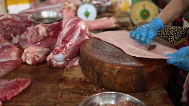 Close-up of a vendor in blue gloves scraping, shaving and preparing raw pork skin on a wooden chopping block at Xom Moi Market in Nha Trang, Vietnam. Commercial food supply and retail butchery trade.
