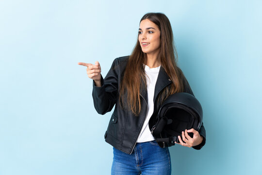 Young caucasian woman holding a motorcycle helmet isolated on blue background pointing finger to the side and presenting a product