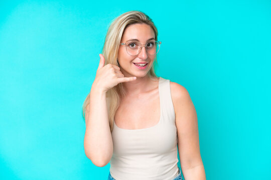 Young caucasian woman isolated on blue background With glasses and doing phone gesture
