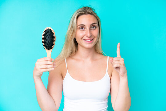 Young caucasian woman with hair comb isolated on blue background pointing up a great idea